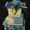 3 tier square blue cake. Base tier is made of fondant cut outs placed in a geomectric design. The middle tier is the blue and white fondant made into a marble design. Flowers are: Lillies, Orchids, Lily of the Valley and an assortment of different flowers